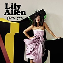 Lily Allen standing behind a set of letters with one hand sitting on top of a letter.