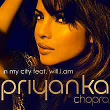 A photograph showing the face of a young, Indian woman from the left profile against a black background. At the foot of the image are the words "In My City feat. will.i.am " and "Priyanka".