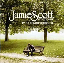 A person sitting on a bench in a park; the person is leaning forward and looking down. The name of the artist and album are written on the top of the picture, imposed over the trees.