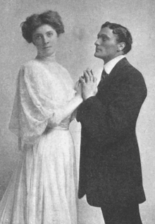 young white couple in Edwardian dress; they are clasping hands lovingly