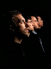 Four men face to the right in profile position with a dark background behind them