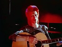 A red-haired man with a guitar against a red backdrop