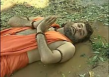 Television snapshot showing man lying down and looking up, hands folded in front of his chest