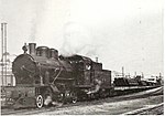 קטר 153 בראש רכבת משא על מסילה צרה עם מטען צינורות נפט, בחיפה בשנת 1946 לערך