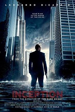 A man in a suit with is back turned and a gun in his right hand, against a cityscape with water coming up to his knees.