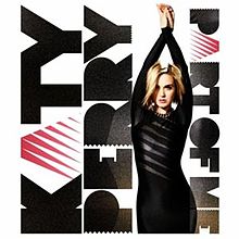 Image shows Katy Perry standing in front of a white background, with her arms interlocked above her head, in a black dress. On her left side, the words "Katy Perry" is written in bold, while on her right "Part of Me" is written in the same format, in a smaller text size.