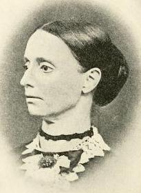 A white woman with dark hair, parted center and dressed back into a large bun. She is wearing a lace collar.