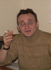 Oleg Bogayev, seated, smoking a cigarette