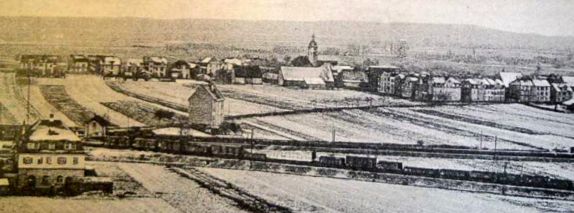 Oberndorf in den 1910er Jahren, im Hintergrund der Steigerwald. Die Bahnstrecke nach Erfurt (vorne) bildet die Grenze zwischen den heutige Stadtteilen Oberndorf und Bergl. Die Bahnstrecke unmittelbar dahinter führt nach Würzburg. Vorne links das Oberndorfer Wasserhaus von 1911 und am rechten Ortsrand der Häuserblock Kornstraße/Bismarckstraße (heute Engelbert-Fries-Straße). Unmittelbar links des Hauses links der Bildmitte verläuft heute die Franz-Josef-Strauß-Brücke (Bahnüberführung).