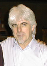 Middle-aged man with white hair and dark eyebrows, wearing a white button up shirt.