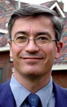 Caucasian man with dark hair and glasses wearing a suit outdoors