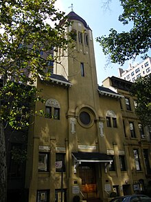 A yellow building with a tower rising from the center, topped by a conical red roof.