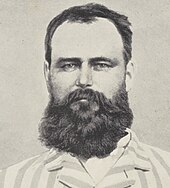 Black and white photograph of the head and shoulders of a bearded man wearing a striped top