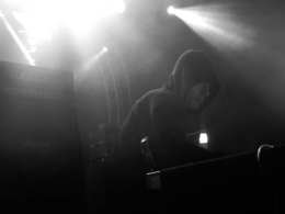 Justin Broadrick in a hoodie holding a guitar next to a Marshall amplifier