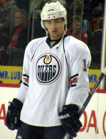 An ice hockey player standing while in a white Edmonton Oilers jersey