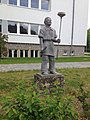 Skulptur „Glasbläserlehrling“, in der betreffenden Berufsfachschule dahinter Glasfenster mit Gravur eines Glasbläsers