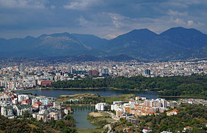 Blick über die Stadt von Süden mit dem Großen Park und dem künstlichen See im Vordergrund und dem Dajti im Hintergrund (2015)