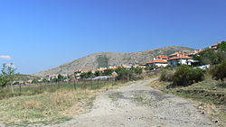 A dirt road looking towards a group of houses with mountains in the background