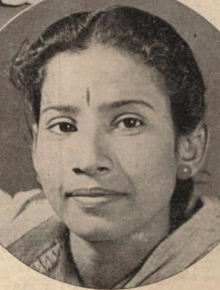 A young South Asian woman, dark hair parted center and dressed back behind her ears; she is wearing a light-coloured shawl