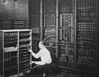 Black-and-white image of a man replacing one vacuum tube out of hundreds in early computer