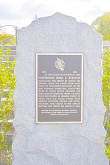 A bronze plaque with gold typeface, on a flat rectangular rock slab.