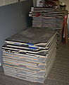 Stacks of plywood-backed billiard table bed slates. The cheaper, darker ones on top are noticeably thinner than the higher-quality light grey ones.