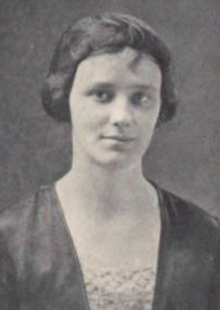 A young white woman with dark hair cut in a short bob, wearing a dark dress or top