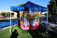 A tent with a sign that says be the voice, stop suicide, and out of the darkness.