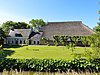 Kop-hals-rompboerderij met voorhuis met omlijste ingang in de lange gevel, dakkapel en twee topschoorstenen met borden