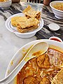 Image 49A bowl of curry mee, with fried beancurd skins and fish cake on the side (from Malaysian cuisine)