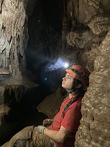 A man sitting inside a tight passageway inside crevice cave, next to several cave formations