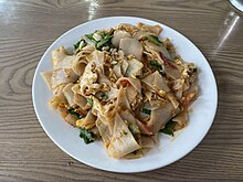 Image of da jiu-ja on a plate. Consists of thinly sliced, square rice cakes with small pieces of egg, peppers and spinach.