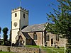 Stone building with lighter coloured square tower. In the foreground are gravestones.