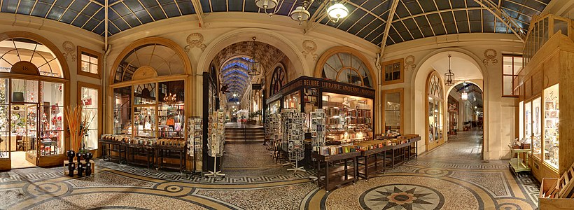 Paris'in en çok bilinen lüks pasajlarından Galerie Vivienne 'da panoramik gönürümü. L'Aparté (no. 46, dekorasyoncu), Jousseaume (no. 48, kitapçı), Martine Rama (no. 54, çerçeveci)'nın dükkanları görülmektedir. Ortadaki koridor rue des Petits Champs girişine ve sağdaki ise rue Vivienne girişine gider. (Üreten: Benh)