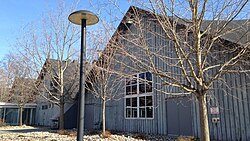 A one-story wood building with a parabolic roof behind leafless trees