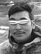 An Inuk wearing traditional snow goggles made from caribou antler with sinew for a strap