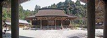 Enclosure of a sanctuary. There is an ablution pavilion, the main wooden building with a thatched roof and a three-storey pagoda. In the background,