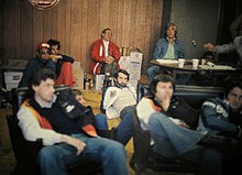 Blick auf eine Gruppe von Fahrern in einem Raum, im Vordergrund Pryce, Jean-Pierre Jarier und Patrick Depailler, im Hintergrund James Hunt, John Watson und weitere Funktionäre