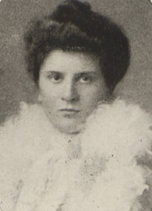 A young white woman with dark hair in a bouffant updo, wearing a fluffy white shawl or stole