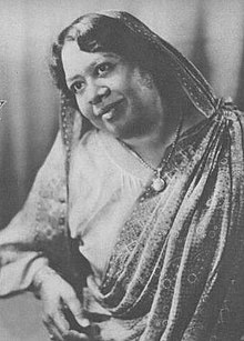 A middle-aged Indian woman wearing a printed sari with the tail draped over her head.