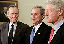 Three men with smiles and greying hair stand together, a painting of Abe Lincoln in the background.