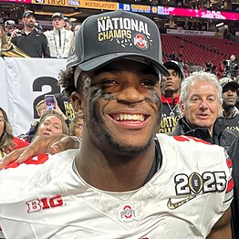 A smiling football player in a baseball hat.