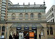 A beige-bricked building with a green sign reading "METROPOLITAN & DISTRICT RAILWAYS GLOUCESTER ROAD STATION" in white letters