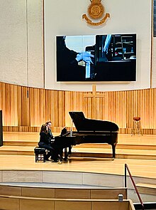 The Ivory Duo Piano Ensemble performing in a recent recital at Regent Hall, London 2023. Behind them a giant screen projects the pianists' hands during the performance.