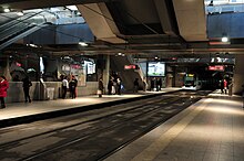 An underground tram stop with a tram arriving at one of the platforms