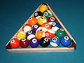 Racking up a game of baseball pocket billiards (racker's view) using an oversized triangle rack for 21 balls. The 1 ball on the foot spot, the 2 on the racker's right corner, the 3 opposite, on the left, and the 9 in the middle of the third row from the apex. All other balls are placed randomly. The balls are (16-21) an Aramith baseball add-on set, and (1-15) Aramith Super Pros.