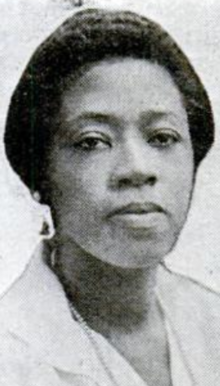 A Black woman with dark hair, wearing a white nurse's uniform