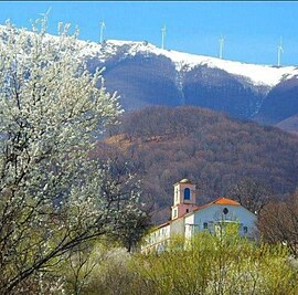 Εκκλησία με καμπαναριό και στο βάθος δεντρόφυτος λόφος και χιονισμένα βουνά.