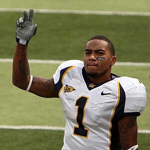 A football player with a white jersey waving towards the camera.