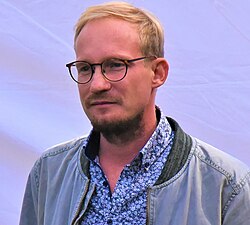 wearing a jacket and a flower-patterned shirt, looking right of camera